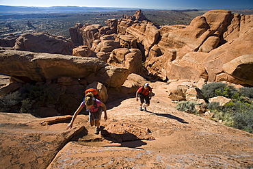 A man and woman hiking in a rocky slickrock area, Arches National Park, Moab, Utah.