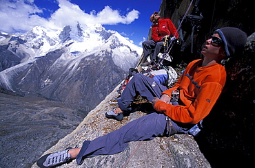 A man and a young male resting on a ledge while climbing in Cordillera Blanca, Peru.