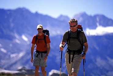 Two hikers trekking through an alpine meadow in Eastern Sierra Nevada mountains, California.