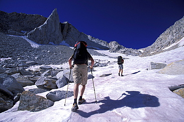 Two backpackers hiking up a snow covered slope in Eastern Sierra Nevada mountains, California.