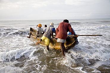 Fishermen pushing a boat into the ocean in Ghana