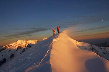 Two mountaineers at the top of a peak in Switzerland at sunset.