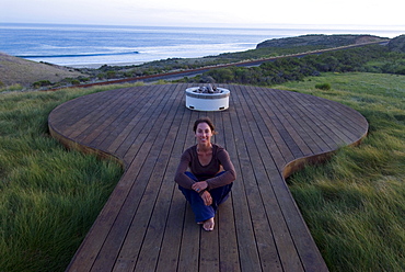 A yong woman watches the sunset from a deck overlooking the Pacific Ocean at Hollister Ranch, California.