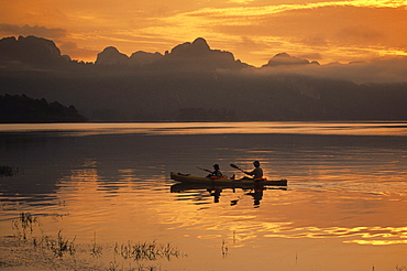 Two people paddle a tandem sea kayak in Khao Sok National Park, Thailand.