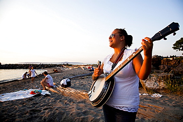 A woman plays the banjo at sunset at a state park beach.