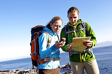 Katrin Schneider and Susann Scheller checking a handheld GPS device while hiking on an ocean trail between Gansbaai and De Kelders. South Africa.