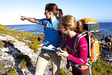 Katrin Schneider and Susann Scheller checking a handheld GPS device while hiking on an ocean trail between Gansbaai and De Kelders. South Africa.