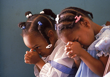 With heads bowed in silent prayer, two young African American girls show worship in a Liberty City, Florida church.