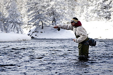 A fly fisherman standing in the river on a winter day.