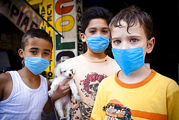 Portrait of three kids wearing masks  holding a small puppy in the street during the swine flu epidemic in Mexico city, DF, Mexi