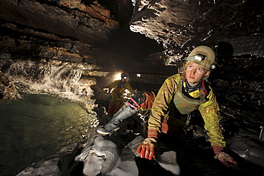 Two explorers crawl past along a ledge in a cave in China.