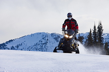 A man rides a snowmobile in a standing position through the snow on Owlshead Mountain.