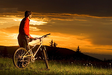 A man standing by his mountain bike watching a colorful sunset from Sargents Mesa on the Colorado Trail in Colorado.