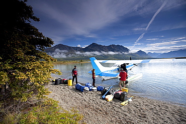 Two men and one woman unload gear from a plane on a lake in Alaska.