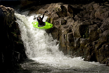 Kayaker launching off of a medium sized drop  while being lit by a strobe.