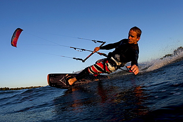 Low angle perspective of a kiteboarder carving by in nice light.