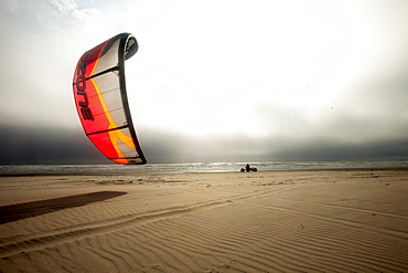 Silhouette of one male kite buggier (kite buggy) rolling down the beach in ominous clouds and unusual light.