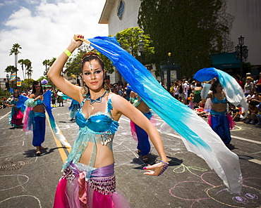 A harem dances up the street at a parade in Santa Barbara. The parade features extravagant floats and costumes.