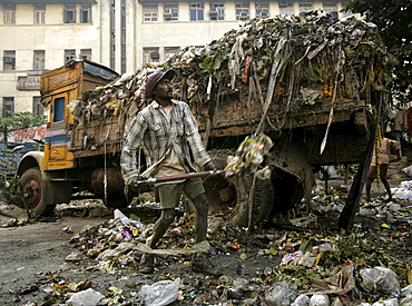 A garbage man shovels garbage into an impossibly over loaded garbage truck at dawn in Kolkata, West Bengal, India