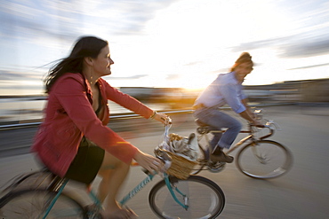 A young man and woman smile as they enjoy a sunny afternoon bike ride through an open street in Portland, ME. (Motion Blur)