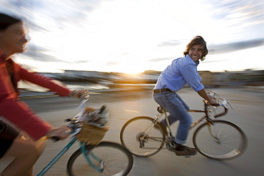 A young man and woman smile as they enjoy a sunny afternoon bike ride through an open street in Portland, ME. (Motion Blur)