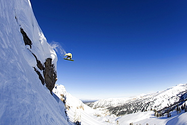 A male snowboarder rides off a 50 foot cliff in the Wyoming Backountry.