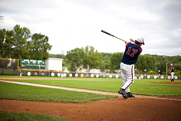 A baseball player swings a bat and hits a practice ball to an outfielder.