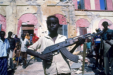 Young boy shows a gun in front of bullet riddled building in Mogadishu, Somalia.