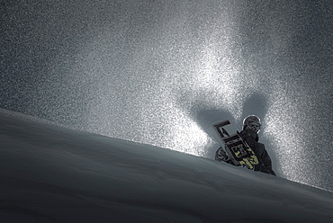 Portrait of backlit snowboarder standing with board on horizon.