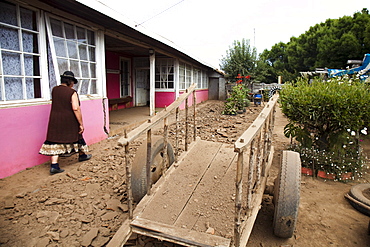 A local woman walks along a beaten dirt path next to a long building in Chile.