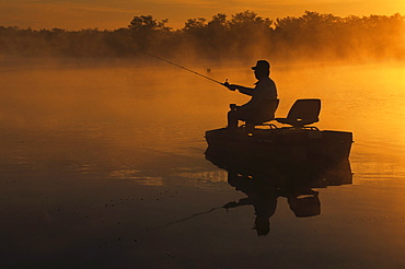 A man bass fishing on the lake at dawn with fog rising off of the lake in southern Illinois.