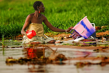 A Songhai woman kneeling in mud washing clothes in the Niger River, Gao, Mali, West Africa