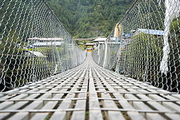 One of the many passageways across deep ravines and over rivers trekking in Nepal.  A suspension bridge made of aluminum, steel cables, and chain link fencing.