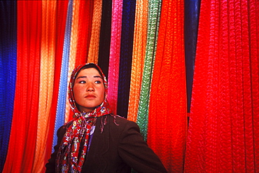 A young woman stands in a fabric stall in a market in Kashgar, China.