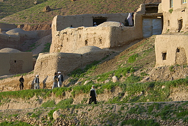 Men walk along a road at dusk, past mud homes in the Tajik village of Dera Jawal, in the Band-e Baba range, Herat Province, Afghanistan