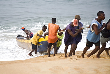 Group of young men pulling a fishing boat out of the ocean. Sulima is a fishing village on the Alantic coast at the mouth of the Moa River near the Liberian border.  Along its pristine beach, one of the longest in West Africa, fishermen launch dugout canoes and fish with nets drag back manually from the shore. Larger power boats mainly from Ghana leave from the more sheltered harbour on the Moa River. Most of the fish is smoke dried by the women of the village and then sold in markets as far off as Monrovia, Liberia.