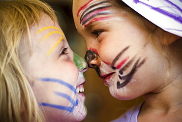 Two girls (2-4 years) decorated in face paint touch nose to nose.