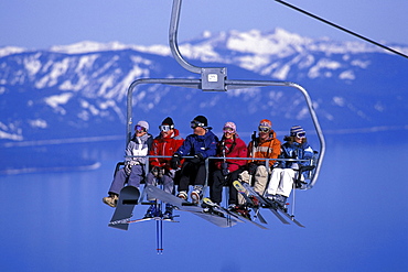 Ski and snowboard buddies enjoy their chairlift ride high above blue Lake Tahoe while skiing at Heavenly Mountain Resort in South Lake Tahoe, California.