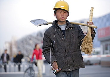 A young migrant worker listens to music on a mp3 player as he walks back to his dorm after a day of work on the Olympic venues, Beijing, China.