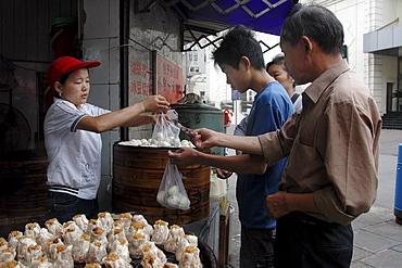 Customers queue up to buy dim-sum style snack foods at a street corner food kitchen near Beijing Dong Lu, central Shanghai, China. In the foreground are shu mei - thin skinned, filled with rice and usually diced pork.