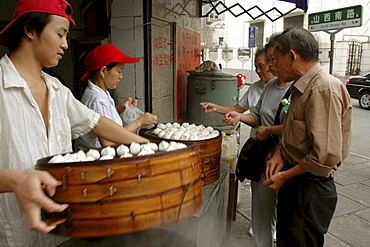 Customers queue up to buy dim-sum style snack foods at a street corner food kitchen near Beijing Dong Lu, central Shanghai, China.