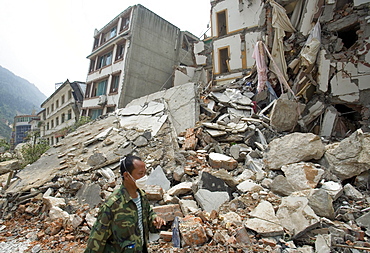 A man walks past a collapsed building in Beichuan Town, which was severely damaged by a powerful 7.9 earthquake. The Chinese government raised the death toll to 21,500 but has said fatalities could rise above 50,000. Tens of thousands could still be buried in collapsed buildings in Sichuan province, where the quake was centered.