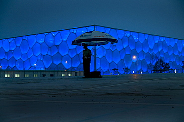 CHINA/Beijing/National Aquatic Center/17June2008:A soldier stands guard outside the National Aquatic Center at night. Designed by Australia's PTW Architects, its facade appearing as a cube of soap bubbles, it seats 17,000 people. The exterior is made from a high-tech lightweight translucent plastic that is also very energy efficient in saving an estimated 30% in power consumption by comparison to a traditional design. It houses 5 pools - one able to create it's own waves. It's outer surface looks like soap bubbles. It will host all swimming and diving events at the 2008 Olympics.