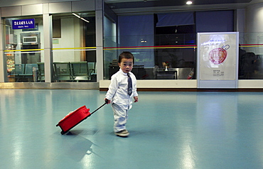 A little boy dressed in a tie pulls a suitcase in the Nanjing airport.