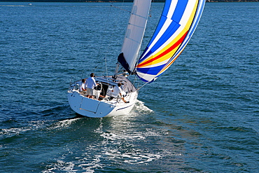 Aerial view of a sailing yacht with a colorful spinnaker cruising in Pittwater on the North Shore from Sydney, Australia.