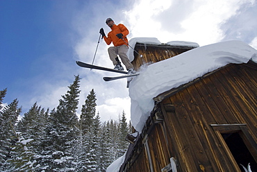 A man jumping off an old mining building  roof with skis in Uncompaghre National Forest, Ouray, Colorado.