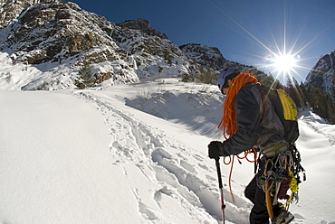 A young man walking in snow and sun with ice climbing gear and rope in Colorado.