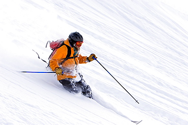 A male telemark skier makes a turn in fresh powder.