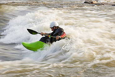 A male whitewater kayaker front surfs his boat.