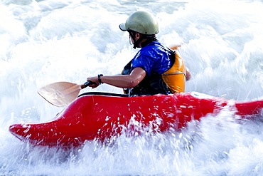 A female kayaker in a playboat battles the rapids of Brennan's Wave on the Clark Fork River, Missoula, Montana.